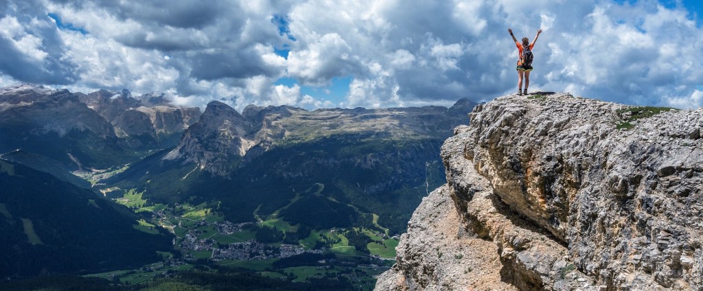 Persona levantando los brazos en la cima de una montaña.